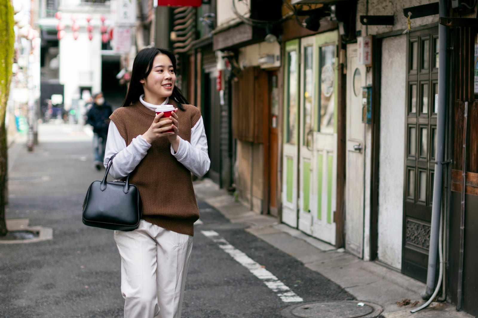 コーヒーを片手に路地を歩く女性