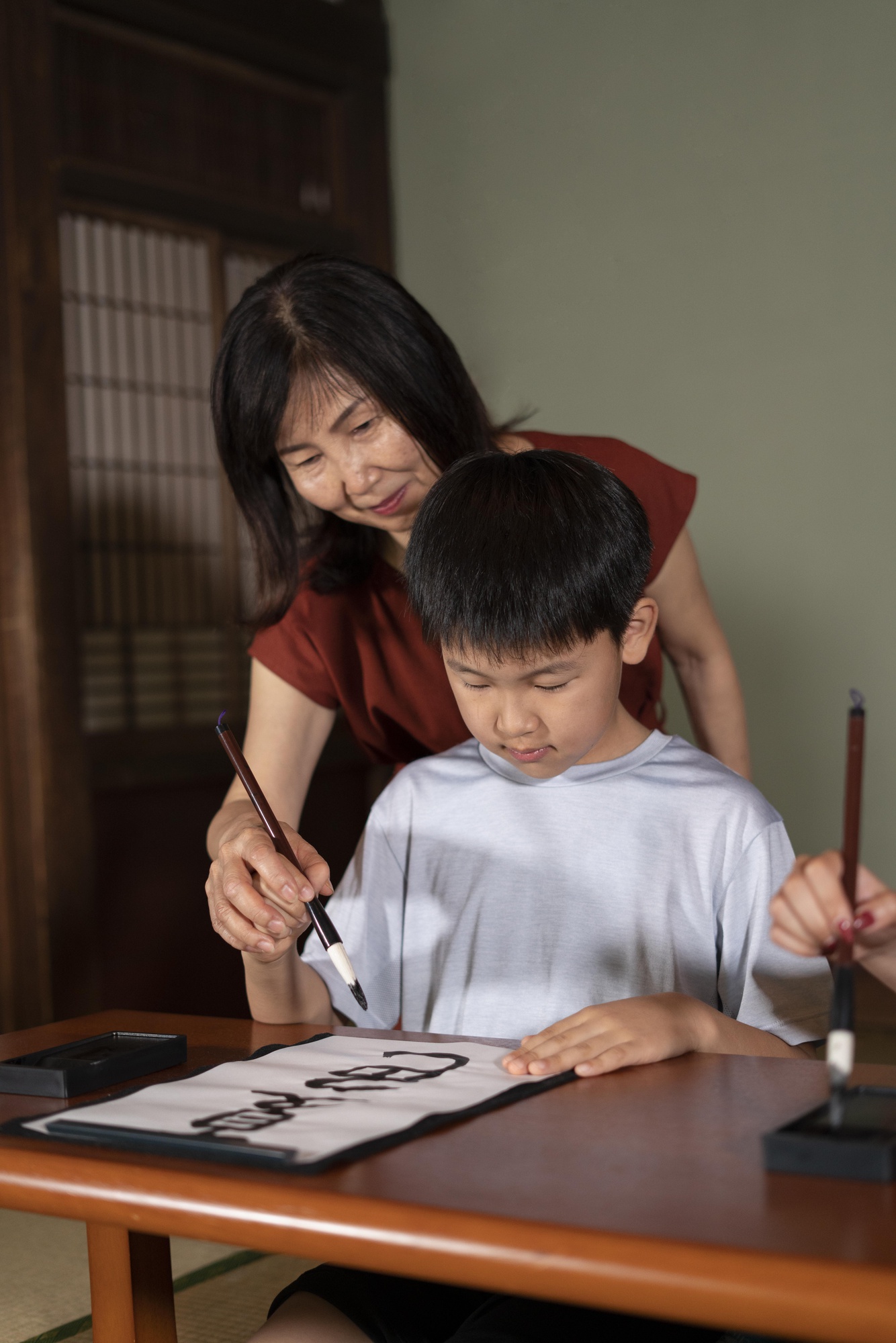 畳の部屋で書道を教わる子どもと先生
